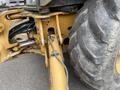 Close-up view of a 2012 John Deere 310SJ backhoe loader highlighting the large rear tire and hydraulic connections on the machine's frame