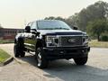 A 2021 Ford F-350 SD with a shiny black exterior large front grille and oversized tires is parked on a roadway