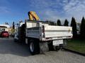 A 2013 International DuraStar 4300 tow truck with a yellow crane arm mounted on the back and a flatbed design