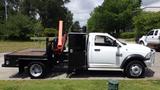 A white 2014 RAM 5500 flatbed truck with a black tool compartment and an orange hydraulic lift on the side