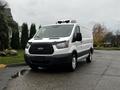 A 2016 Ford Transit van with a white exterior and black front grille parked on a wet surface