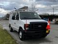 A white 2011 Ford Econoline van with a roof rack and orange traffic cones attached to the front headlights