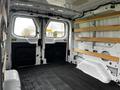 The interior of a 2023 Ford Transit showing a spacious cargo area with two bench-style wooden shelves and a black rubber floor mat