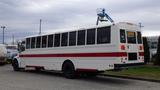 A white 2013 Freightliner M2 106 bus with red stripes on the side parked with windows along the length and large rear lights