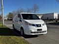 A white 2017 Nissan NV200 van parked on the street with a simple front design and sliding side door