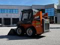 A 2017 Gehl R105 skid steer loader with a black and orange exterior and a front bucket attachment parked on a gravel surface