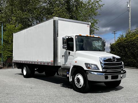 A 2020 Hino 338 truck with a white box cargo area and a black grill is positioned at an angle with its headlights on and five orange lights mounted on the top of the cab