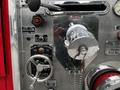 A metal control panel of a 1991 Sutphen Deluge showcasing various levers and gauges along with a shiny relief valve and circular pump control wheel