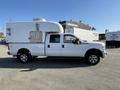 A white 2014 Ford F-350 SD with a large enclosed camper shell mounted on the bed and dual rear wheels