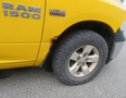 A yellow 2015 RAM 1500 with a damaged wheel well and a flat tire on the front right side