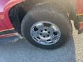 A close-up of a chrome wheel on a red and black 2011 Chevrolet Avalanche with a rugged tire showing tread patterns