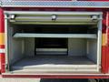 An open storage compartment of a 2004 American LaFrance Eagle fire truck featuring metal shelving and a lined interior