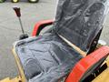 A black seat with plastic covering and a red armrest on a mini loader with a gear shift lever nearby