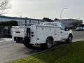 A white 2016 Ford F-350 SD truck with a utility bed and toolboxes on either side, featuring a mesh safety cage and a hitch at the rear