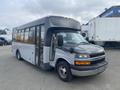 A 2016 Chevrolet Express bus with a gray and black exterior and large windows parked at a commercial location