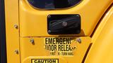 Close-up of a yellow school bus door with a black emergency door release handle and a caution label underneath