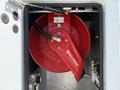 A red hose reel mounted inside a compartment of a vehicle with a metal housing and connecting hoses visible
