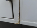 Close-up view of a rusty section on the side of a white 2020 Chevrolet Express van showing paint damage and corrosion along the seam