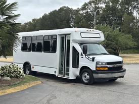 A white 2020 Chevrolet Express bus is parked with its door open, featuring large windows and a modern design