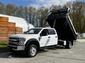 A 2021 Ford F-550 truck with a white cab and a black dump bed raised for unloading