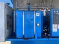A blue hydraulic tank with metal fittings and gauges on a machinery platform, featuring a prominent pressure gauge and various control panels