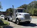 A 2019 Peterbilt 337 truck is parked with a white cab silver grille and exhaust stacks prominently displayed with a flatbed in the rear