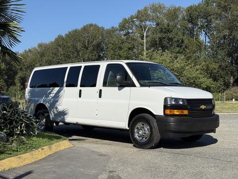A white 2021 Chevrolet Express van with four side windows and alloy wheels parked at a slight angle