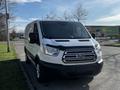 A white 2017 Ford Transit van with a black front grille and multiple windows parked on the street