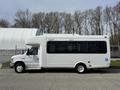 A white 2010 Ford Econoline shuttle bus with large windows and a raised roof featuring a wheelchair accessibility symbol on the side