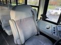 A gray driver's seat of a 2015 International 3000 bus with a seatbelt and a console featuring controls and a cup holder