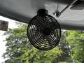 A black metal fan with four blades mounted on a ceiling inside a bus