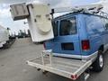 A blue 2010 Ford Econoline van with a bucket lift attached to the rear and a metal ladder rack on the back bumper