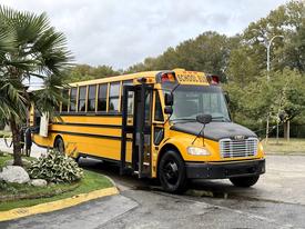 A yellow 2014 Freightliner B2 school bus with large windows and the words SCHOOL BUS displayed on the front