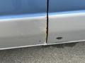 A close-up view of the side of a 2010 Ford Econoline showing rust and paint damage on the lower panels