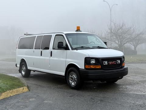 A 2016 GMC Savana van in white with a light on the roof and chrome wheels parked in a foggy area