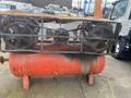 A rusted 2000 Baldor Air compressor featuring two large fans on top of a red air tank with a mesh cover