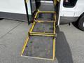A 2018 Chevrolet Express wheelchair ramp extends from the side door with yellow edges and a textured black surface showing signs of wear and some yellow markings