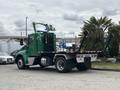 A green 2013 Kenworth T370 with a flatbed and dual rear wheels is seen parked with equipment on the flatbed and a lift attached at the rear
