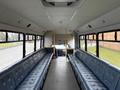 Interior view of a 2011 Ford F-550 bus showing long padded seats on either side with a clear aisle and the driver area visible at the front