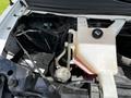Engine compartment of a 2013 Chevrolet Express showing the coolant reservoir and battery with various hoses and electrical components visible