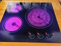 A three burner cooktop with two large and one medium circle glowing in purple and three control knobs with red indicators