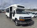 A white 2018 Chevrolet Express bus with a large front windshield and multiple windows on the side is parked with its doors open