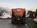 A 2006 Freightliner M2 106 snowplow truck facing away with an orange body and a sign that says Do Not Pass Snowplow