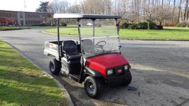 A red 2017 Toro Workman utility vehicle with a black bench seat and a flatbed cargo area parked on a paved surface