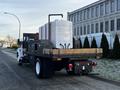 A 2011 Ford F-750 truck with a flatbed carrying two large white tanks and various storage boxes at the back