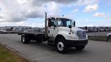 A white 2015 International DuraStar 4300 flatbed truck parked with its front slightly angled and the cab featuring a tall exhaust stack and multiple lights on the roof