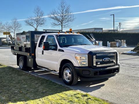 A white 2011 Ford F-350 SD with a flatbed and tool compartment visible in the back is parked with its front facing toward the viewer