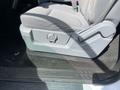 A close-up of the driver's side seat adjustment mechanism in a 2012 Ford F-150 showing a gray knob for reclining and a padded seat in light gray fabric