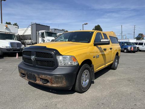 A yellow 2015 RAM 1500 with a black grille and chrome accents parked prominently with some rust on the front bumper