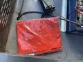 A sealed red blanket wrapped in plastic placed on a textured surface with electrical components nearby